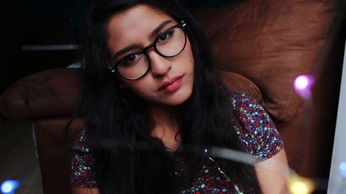 Portrait of young woman wearing eyeglasses while holding string light