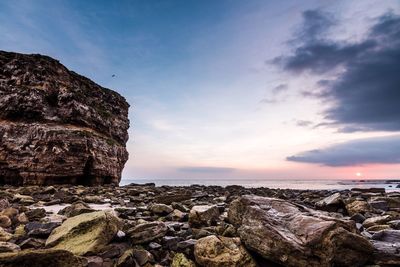 Rock formation by sea against sky during sunset