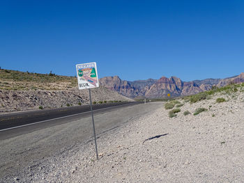 Road sign by landscape against clear blue sky