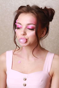 Young woman with pink make-up chewing gum against wall