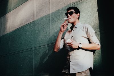 Full length of young man smoking cigarette against wall