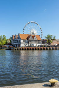 Ferris wheel by the river against clear blue sky