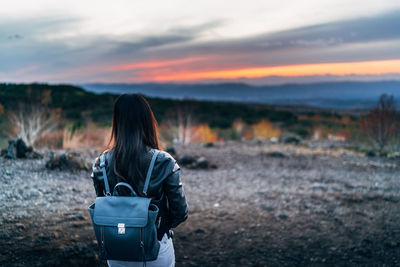 Rear view of woman standing on field against sky during sunset