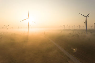 Wind turbines on field against sky during sunset
