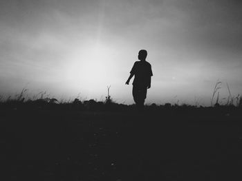 Silhouette man standing on field against sky during sunset