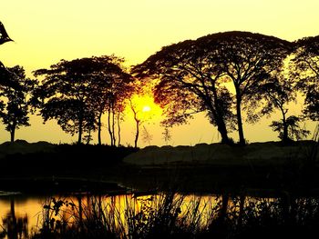 Silhouette trees by lake against sky during sunset