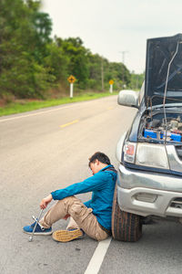 Man sitting by broken down car on road