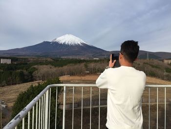 Rear view of man photographing snowcapped mountain against sky