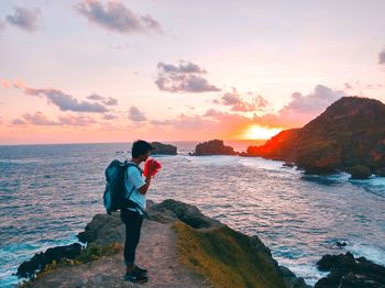 Man standing on rock by sea against sky during sunset