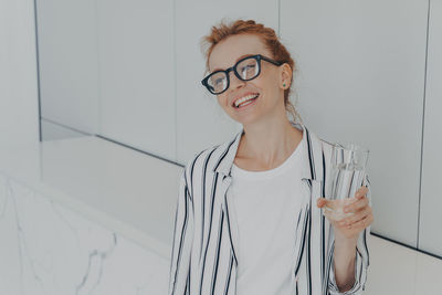 Portrait of smiling young woman standing against wall