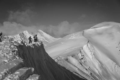 Hikers on rock formation by snowcapped mountains during winter