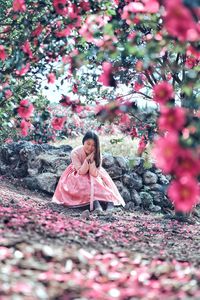 Woman sitting on rocks wearing a pink dress with pink flowering plant in the foreground