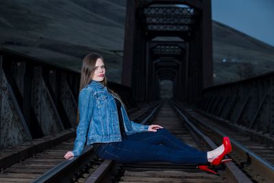Portrait of beautiful young woman sitting on railway bridge at dusk