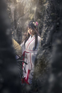 Young woman wearing traditional clothing while standing by tree trunks