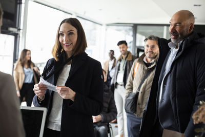 Smiling businesswoman holding id card looking at receptionist in conference center