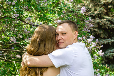 Family portrait of young happy man and woman in each other's arms in blossom spring garden.