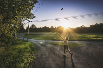 Rear view of boy with arms outstretched catching toy while standing outdoors