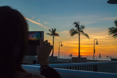 Silhouette of man photographing sea at sunset