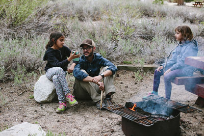 Girl looking at sister showing smart phone to father while sitting at campsite