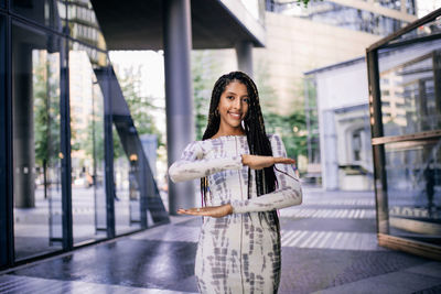 Portrait of young woman with long hair gesturing while standing outside building