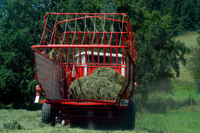 Red tractor with trailer loaded with hay on the field