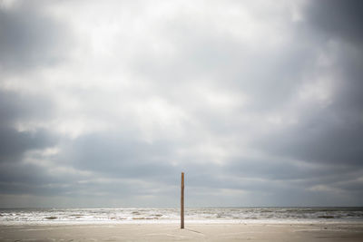 Wooden post on shore at beach against cloudy sky