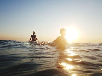 People in sea against sky during sunset