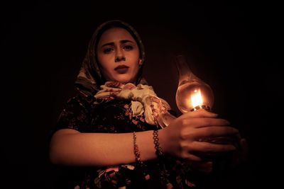 Portrait of woman holding lit lantern in darkroom