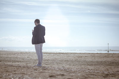 Rear view of man standing on sand at beach against sky