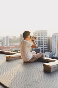 Man sitting in city against sky