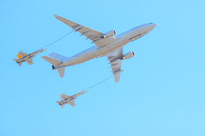 Low angle view of jet fighter airplanes flying engaging in mid-air refueling against clear blue sky