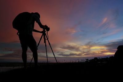 Silhouette man photographing against sky during sunset