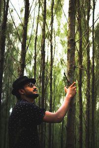 Side view of man standing by tree in forest