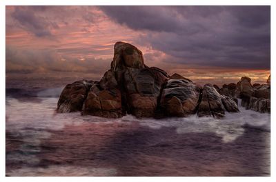 Rock formation in sea against sky during sunset