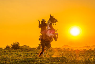 Full length of cow boy riding horse at meadow during sunset