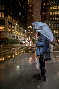 Person holding umbrella on wet street during rainy season