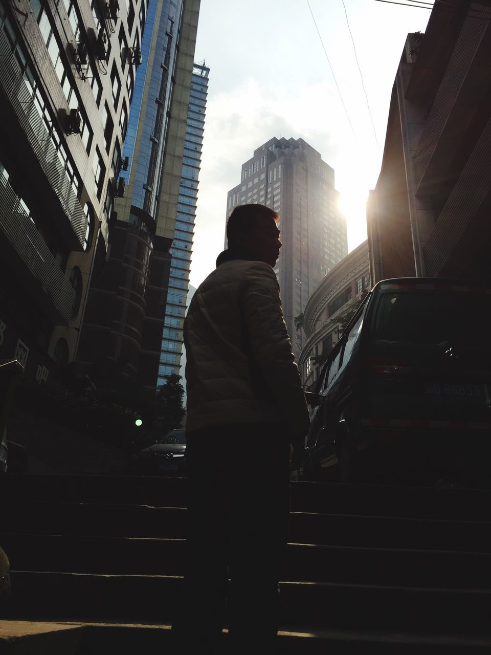 building exterior, architecture, built structure, city, lifestyles, sunlight, men, city life, rear view, leisure activity, building, skyscraper, sunbeam, sky, silhouette, sun, standing, low angle view