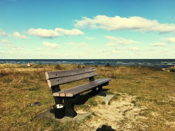 Empty bench on beach against sky