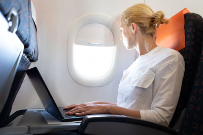 Side view of businesswoman working on laptop sitting at airplane