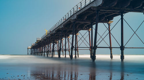 Pier over sea against clear blue sky