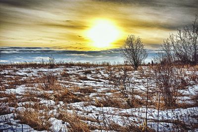 Snow covered landscape against sky during sunset