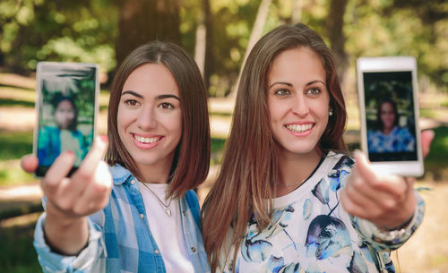 Female friends talking selfie with smart phones at park