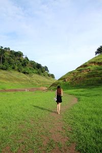 Rear view of woman walking on field against sky