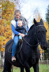 Woman sitting with baby boy on horse at field during autumn