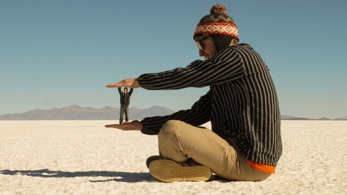 Man sitting on beach against clear sky