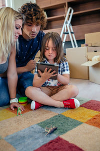 Mother and father looking at son using digital tablet by cardboard boxes at home