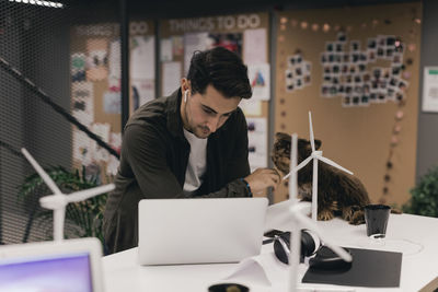 Young businessman using laptop while touching dog at desk in office