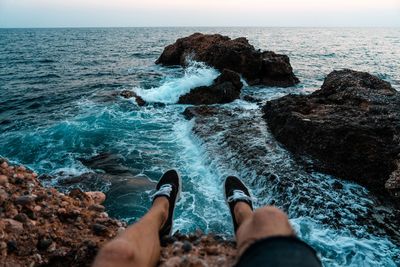 Low section of people on rock in sea against sky