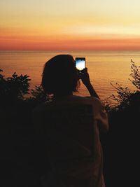 Rear view of woman photographing at sunset