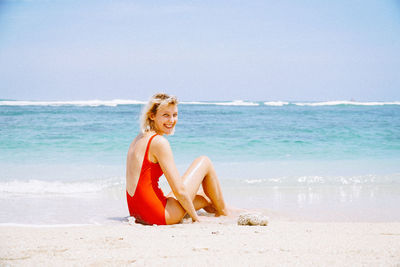 Portrait of smiling young woman sitting on beach against sky